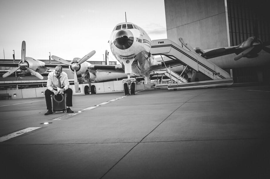Roman Freud sitting on a suitcase on an airfield in front of a vintage airliner