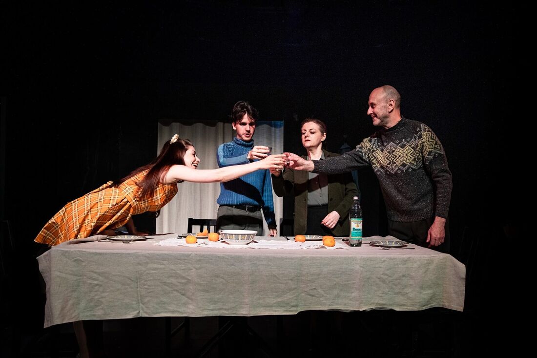 Four actors raise glasses over a long dinner table